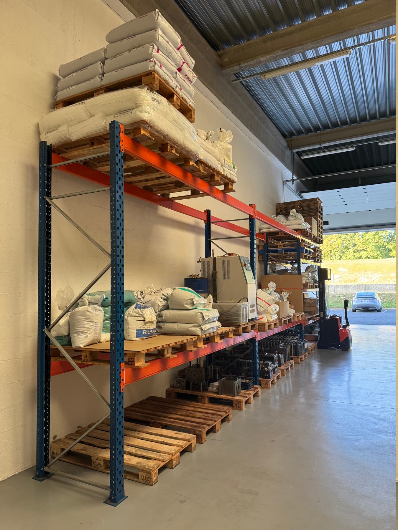 Zone de stockage de l’atelier : rack, palettes de matière et moules au fond