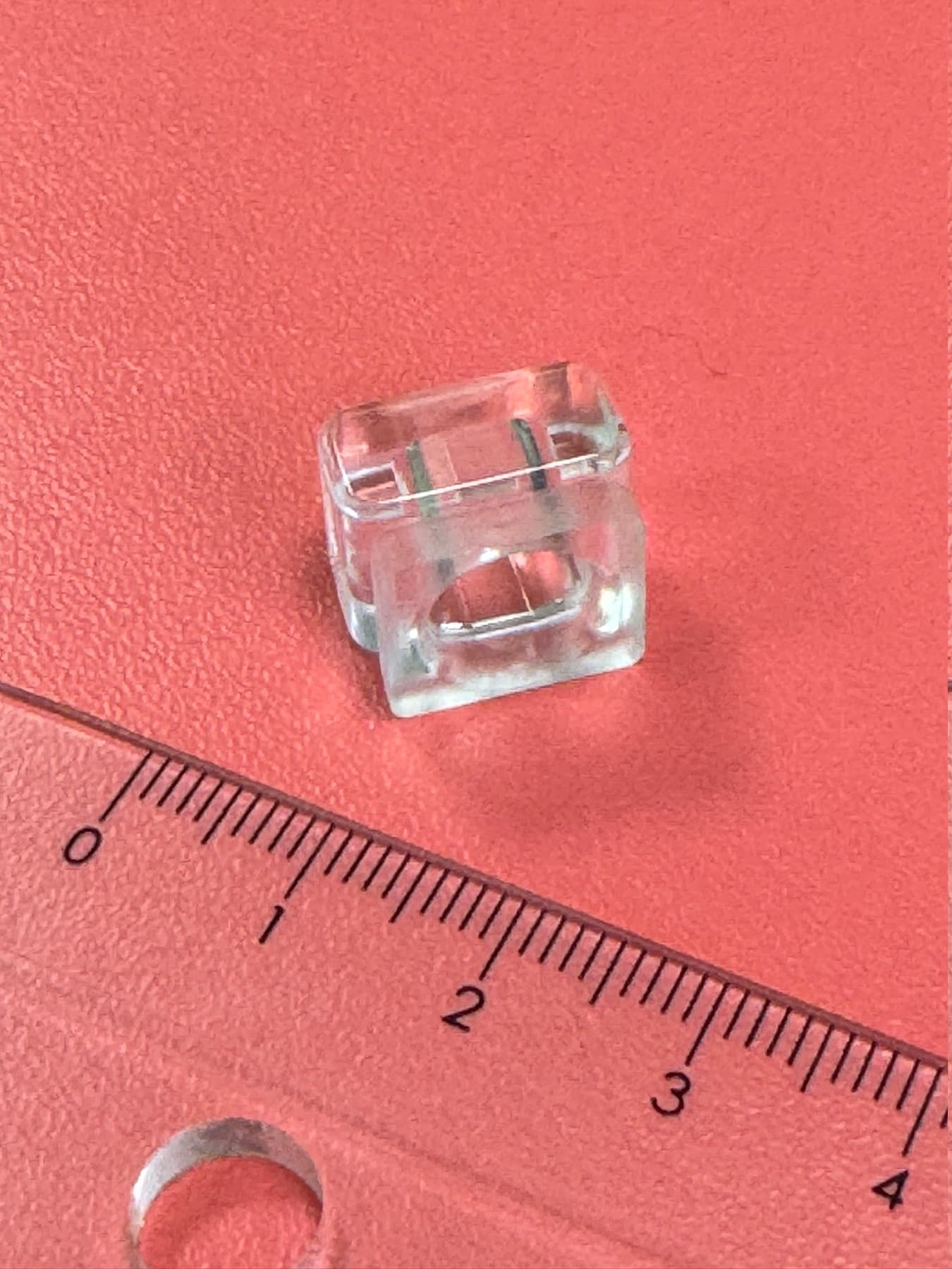 Petit boîtier plastique transparent posé le long d’une règle graduée, environ 1,5 cm
