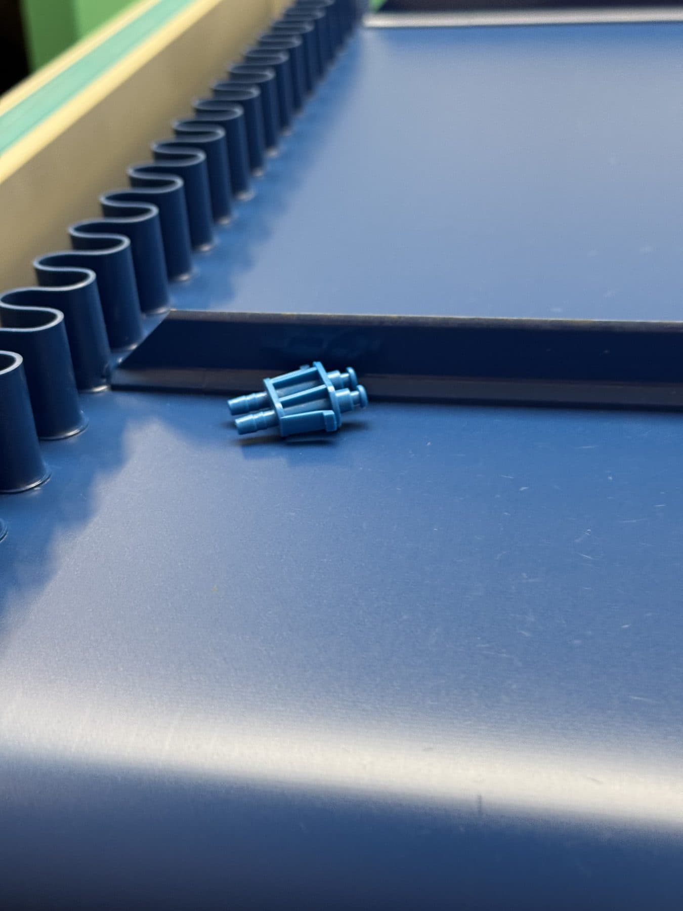 Petit raccord plastique bleu seul sur le tapis d’un convoyeur d’atelier, en sortie de presse